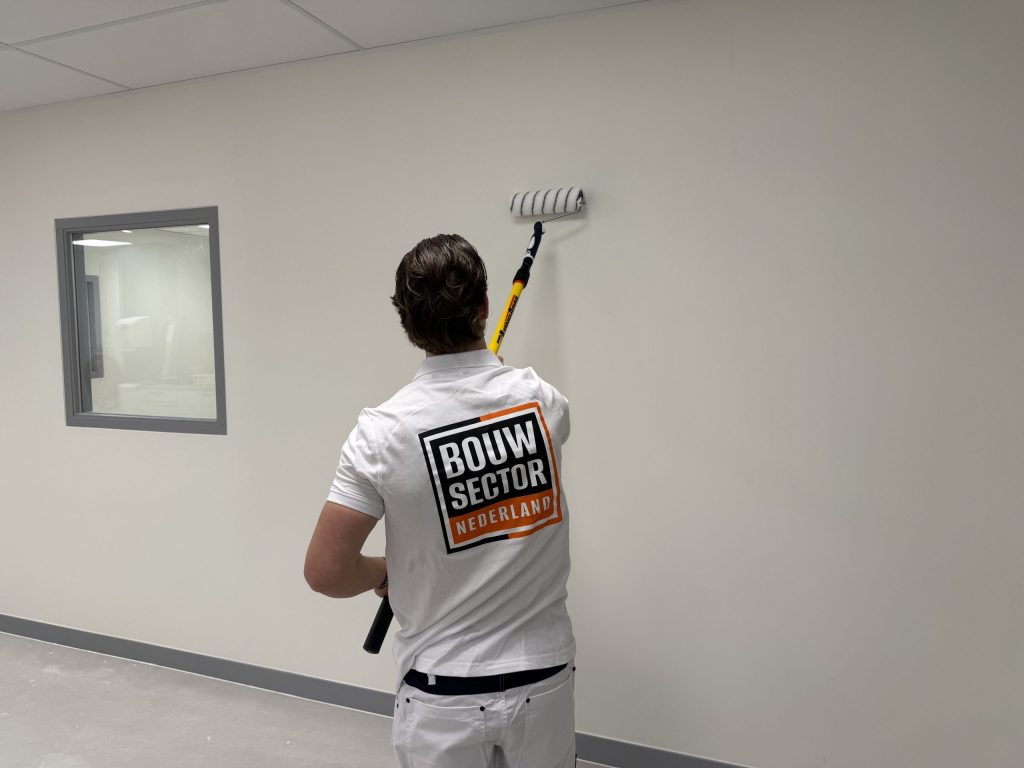 Schilder rolt een witte wand in een lege ruimte met een binnenraam in grijs kozijn