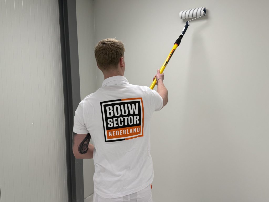 Schilder in wit werkpolo rolt een lichte wand naast een grijze deurpost