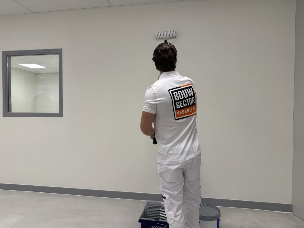 Schilder van Bouwsector Nederland rolt een witte wand bovenaan, verfbak en emmer op de grond